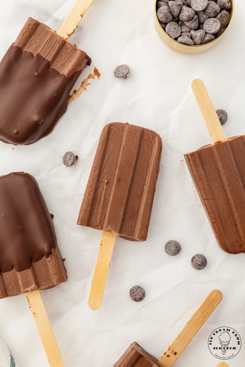 5 chocolate ice cream bars arranged on parchment paper. chocolate chips are strewn about.