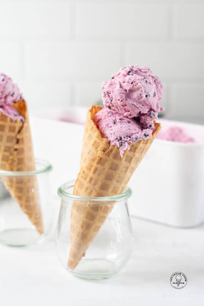Two small jars holding up waffle cones filled with purple huckleberry ice cream.