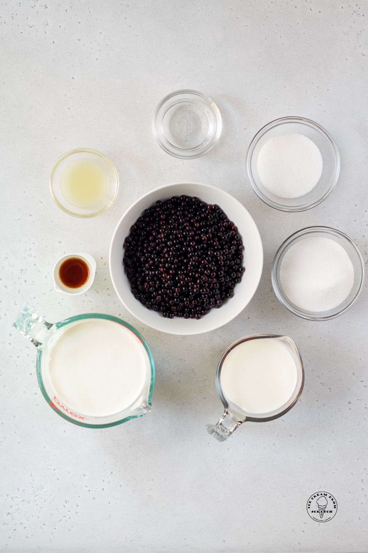 a white bowl filled with huckleberries, surrounded by the other ingredients needed to make huckleberry ice cream.