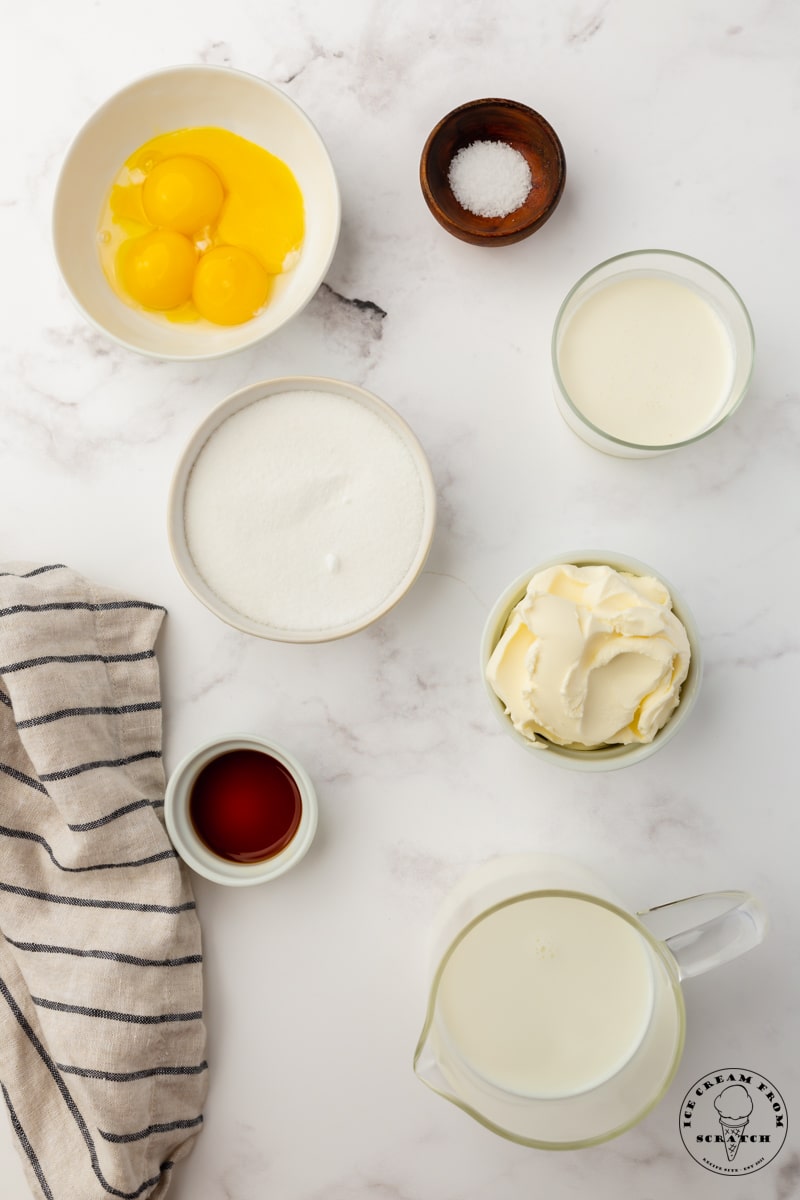 The ingredients in homemade mascarpone ice cream, including egg yolks, cream, sugar, and vanilla. Each ingredient is measured into it's own small bowl and arranged on the counter, viewed from overhead.