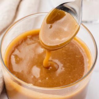 a small glass bowl of homemade caramel sauce with a spoon dipping into it.