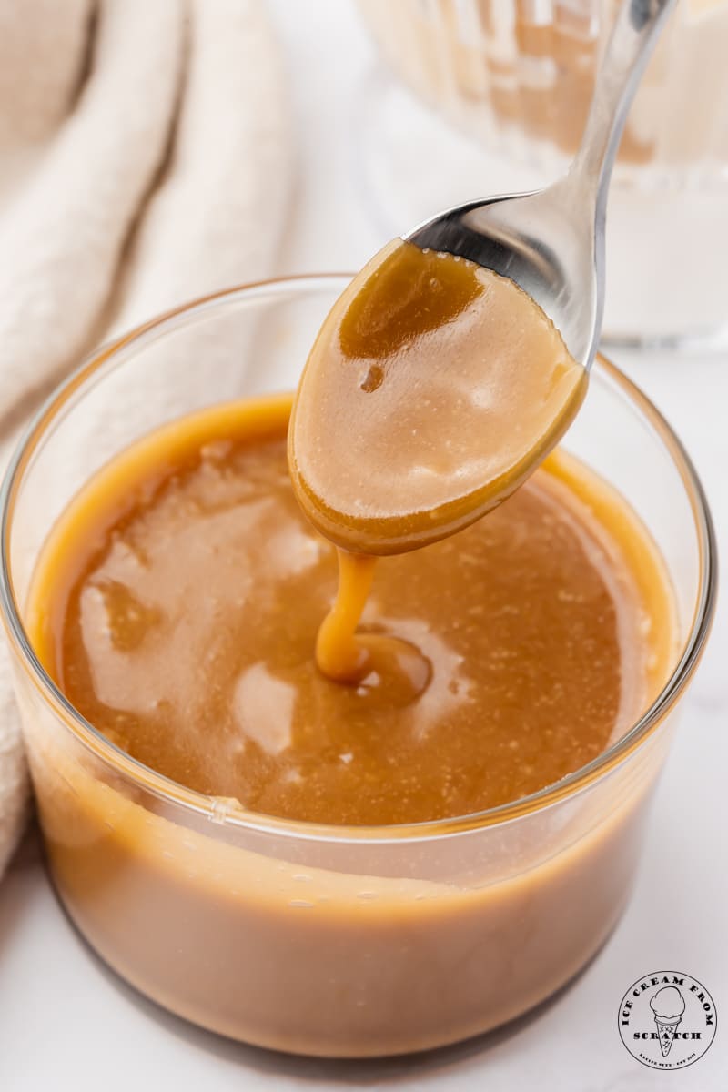 a small glass bowl of homemade caramel sauce with a spoon dipping into it.