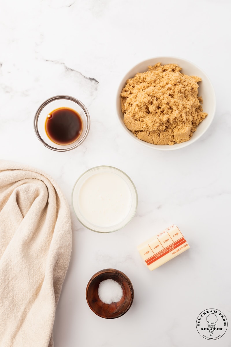 The ingredients needed to make caramel sauce with butter and brown sugar, in separate bowls on a counter.