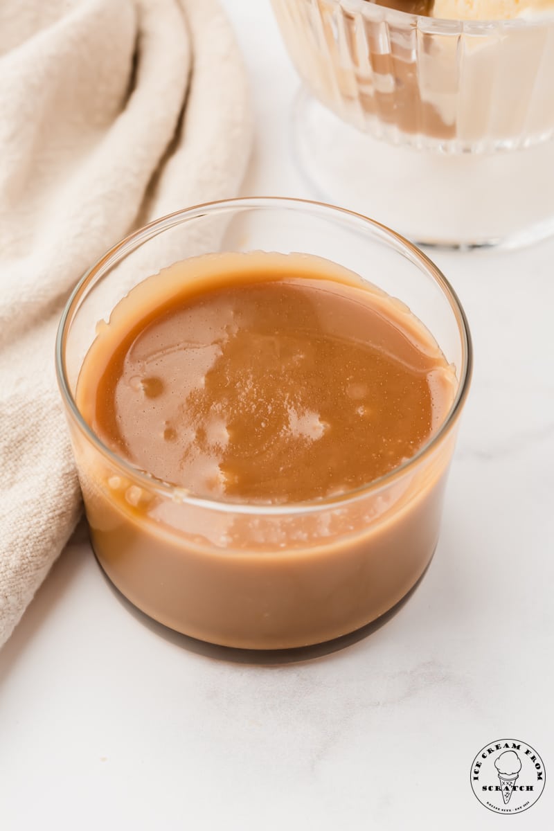 a small glass bowl filled with caramel sauce, on a marble countertop.