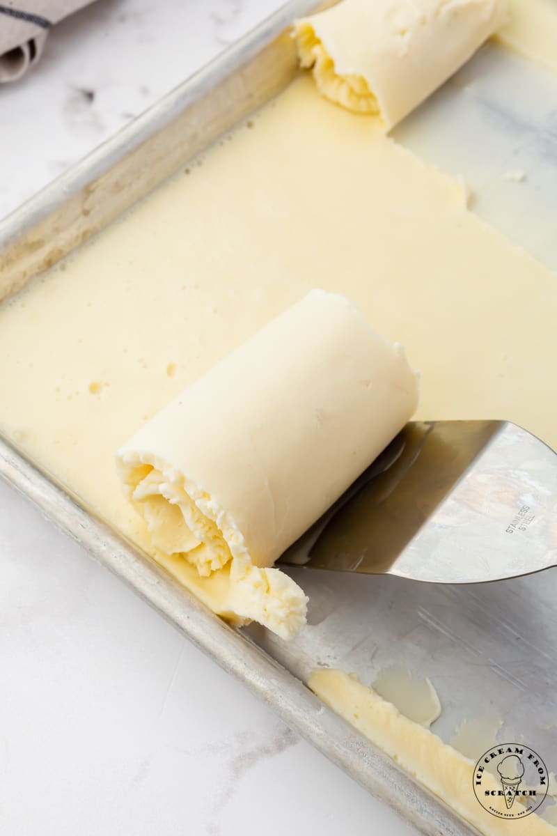 a spatula scraping ice cream rolls off of a sheet pan.