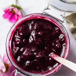 a hinged glass jar of blueberry compote. Purple flowers are seen in the background.