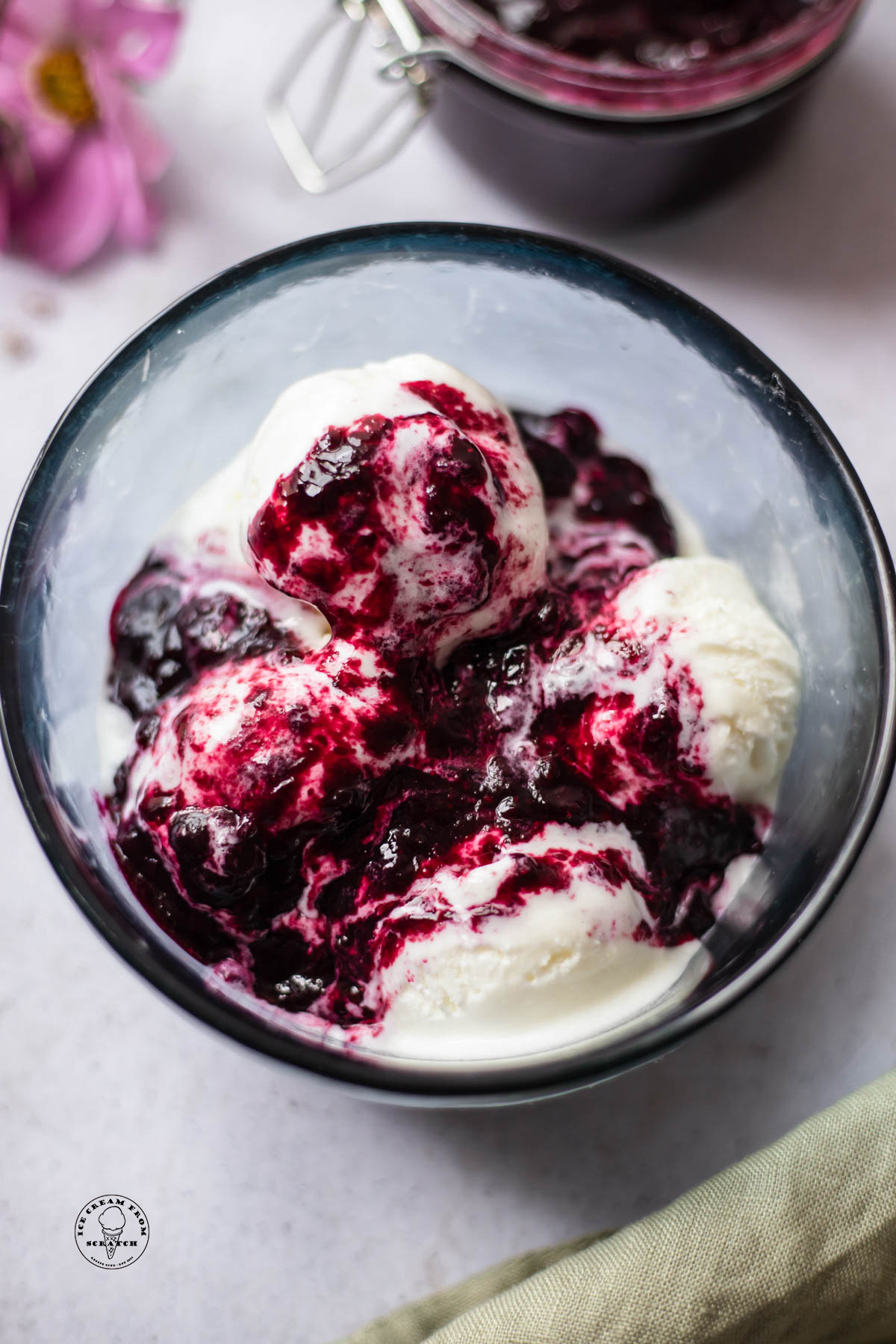 A glass bowl with scoops of vanilla ice cream topped with fresh blueberry compote.