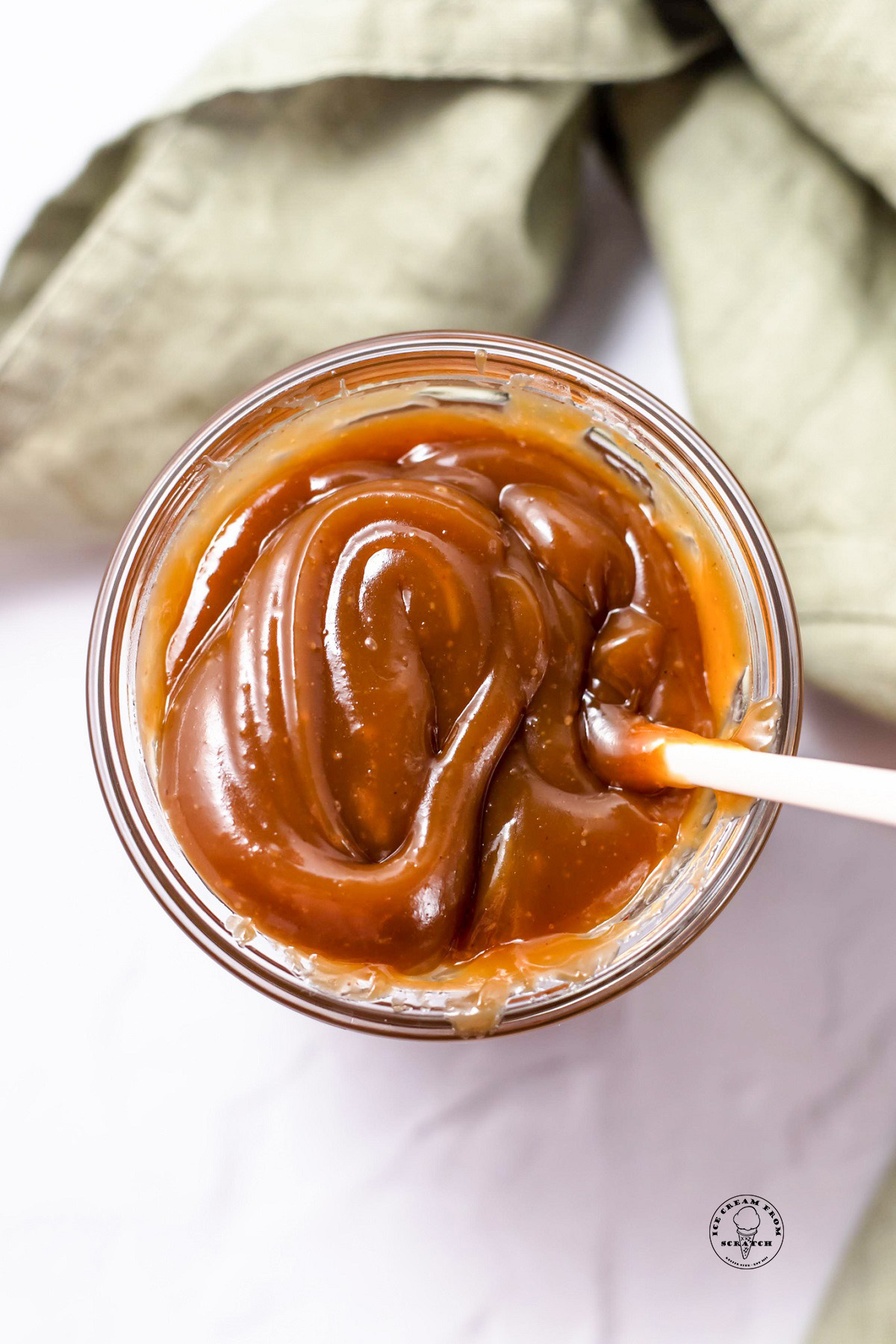 A glass jar of thick peanut butter ice cream sauce, viewed from directly overhead.