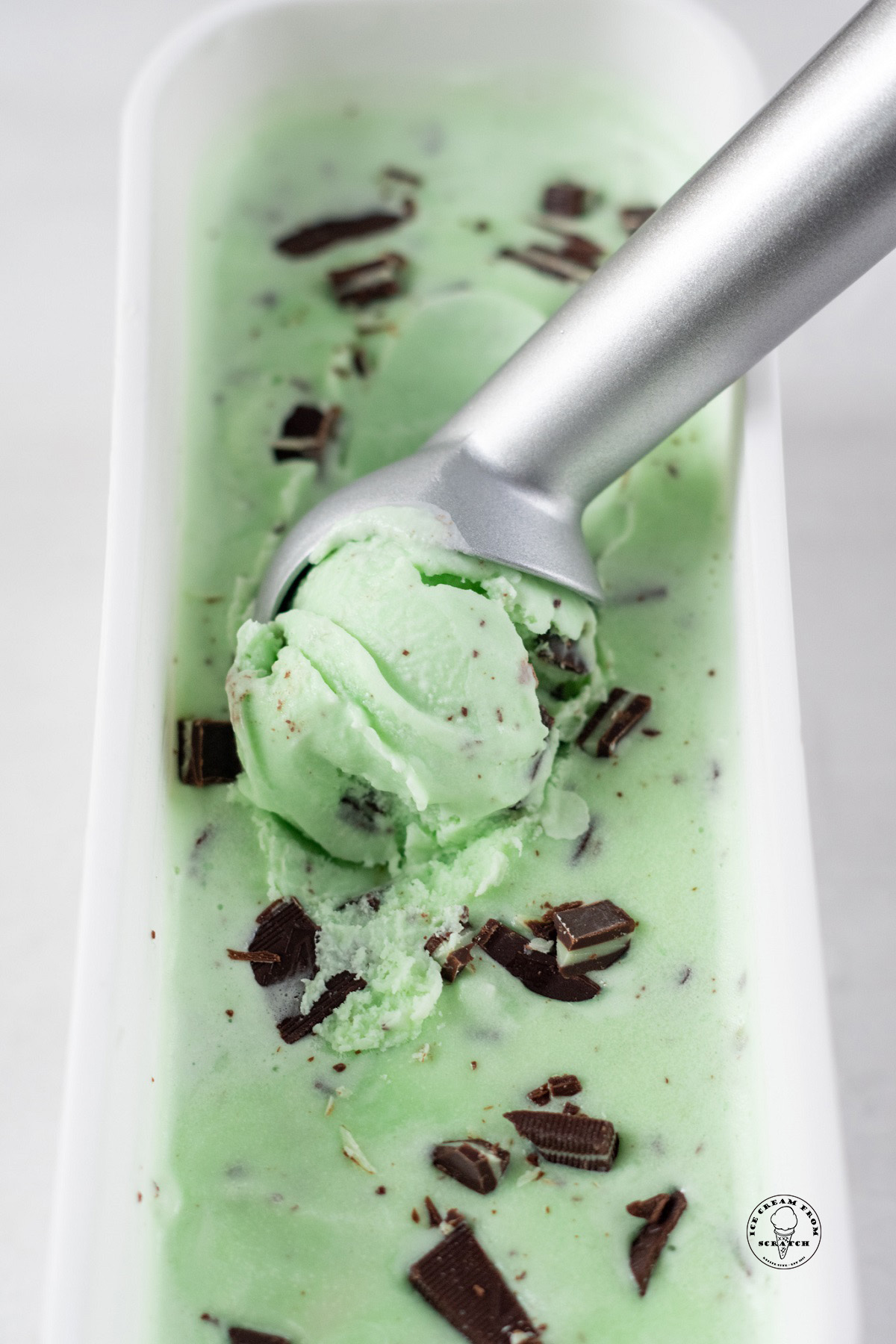 a metal ice cream scoop creating a scoop of homemade andes mint ice cream from a plastic container.