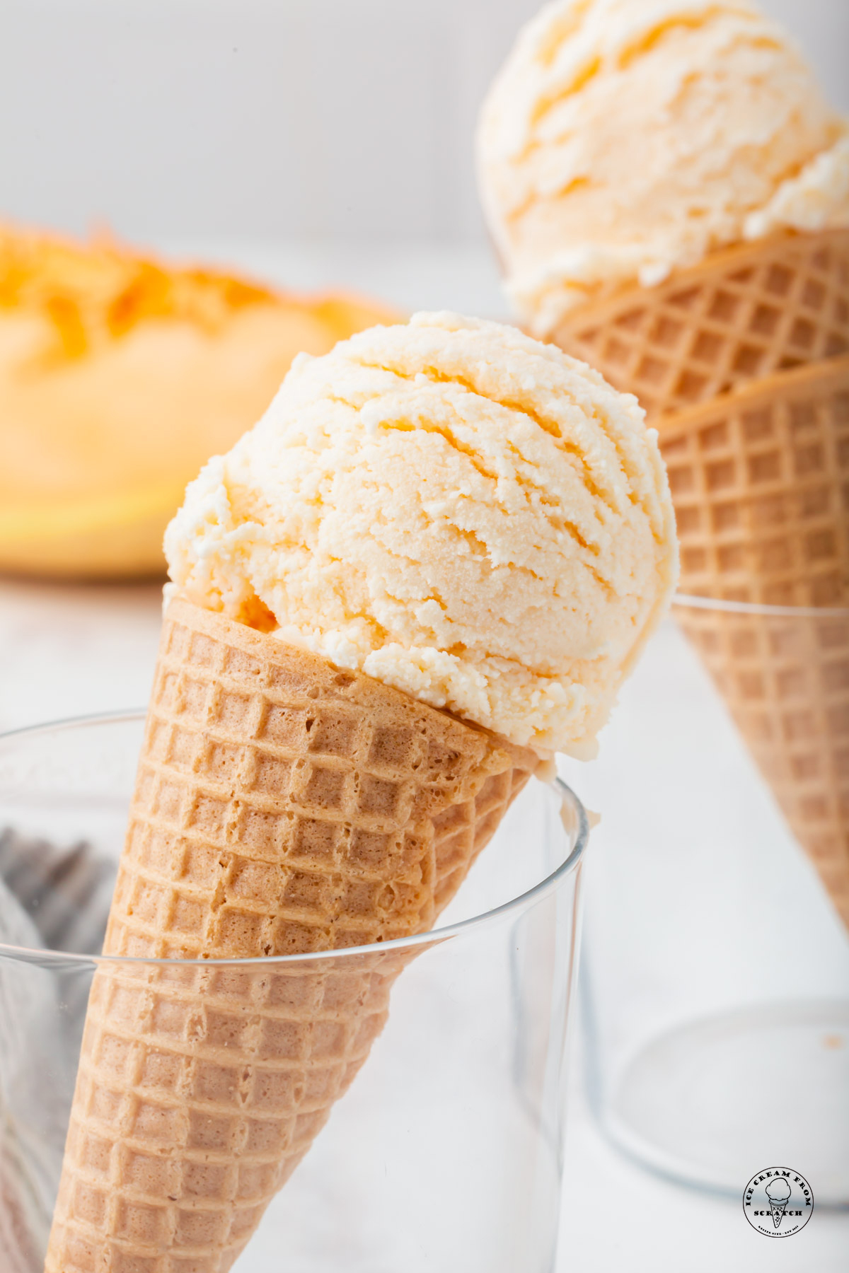 sugar cones topped with scoops of cantaloupe ice cream, propped up in glasses.