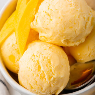 a bowl filled with scoops of mango gelato and mango slices.