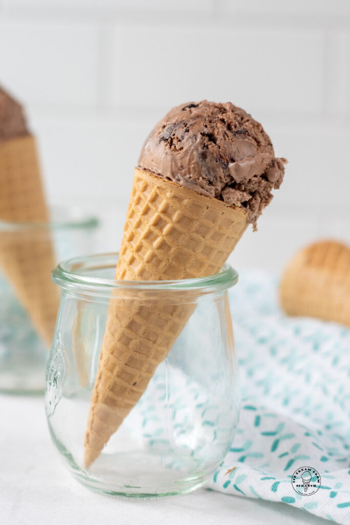 a sugar cone topped with one scoop of chocolate ice cream, held upright in a small jelly jar.