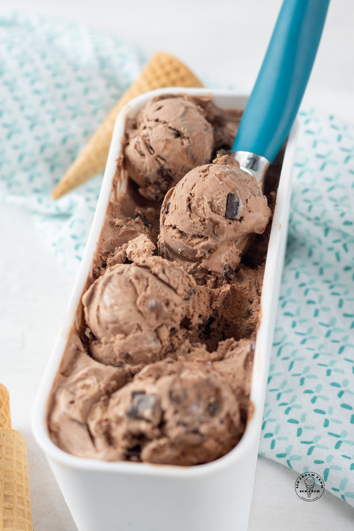 scoops of death by chocolate ice cream in a white container, with a blue-handled ice cream scoop.