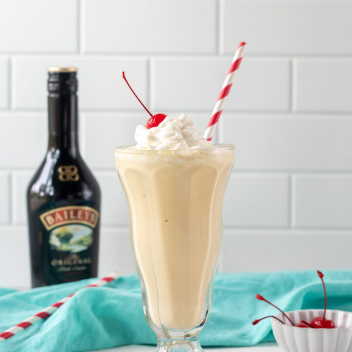 a milkshake in a footed glass with a red and white straw in it, next to a bottle of baileys Irish creme.