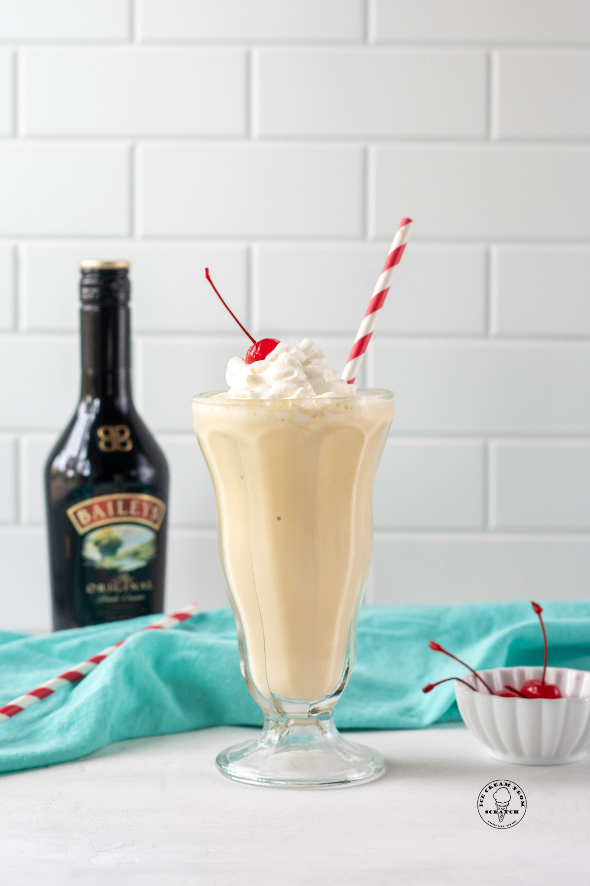 a milkshake in a footed glass with a red and white straw in it, next to a bottle of baileys Irish creme.