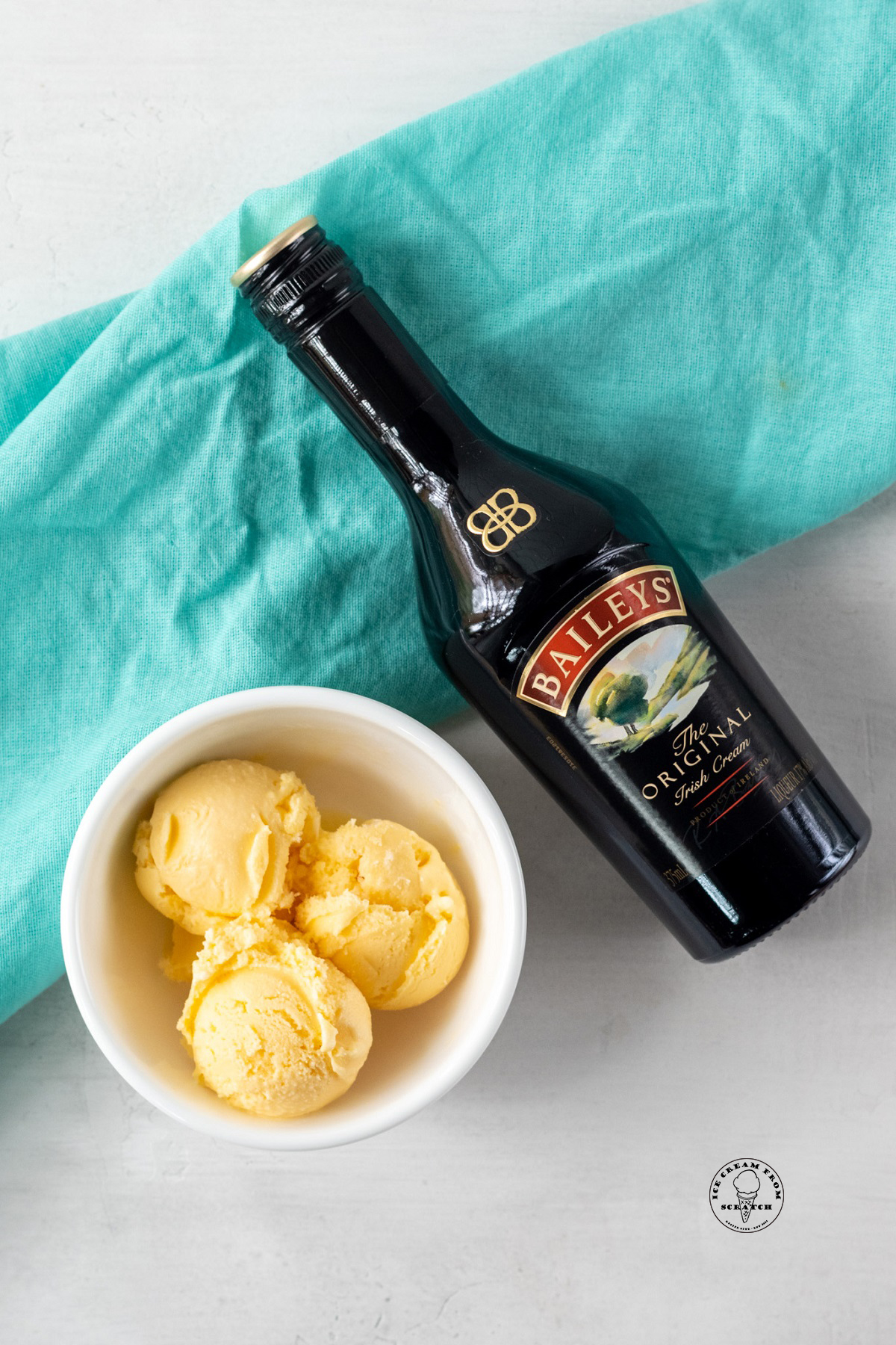 a bottle of baileys irish cream next to a bowl of vanilla ice cream.