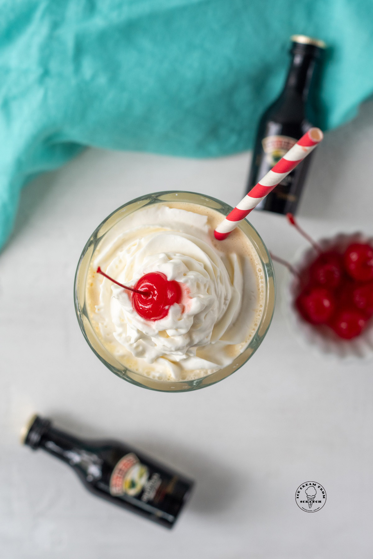 a bailey's milkshake topped with whipped cream and a cherry, viewed from above. Small bottles of liqueur are in the background.