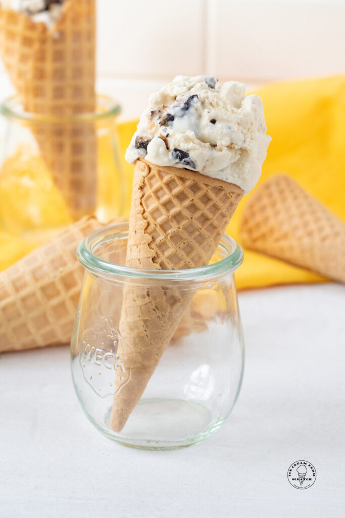 a scoop of homemade butter brickle ice cream on a sugar cone, propped up in a small jelly jar.