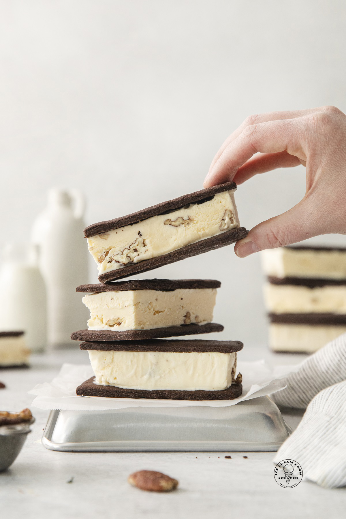 Three homemade pecan ice cream sandwiches. A hand is grabbing on from the top of the stack.