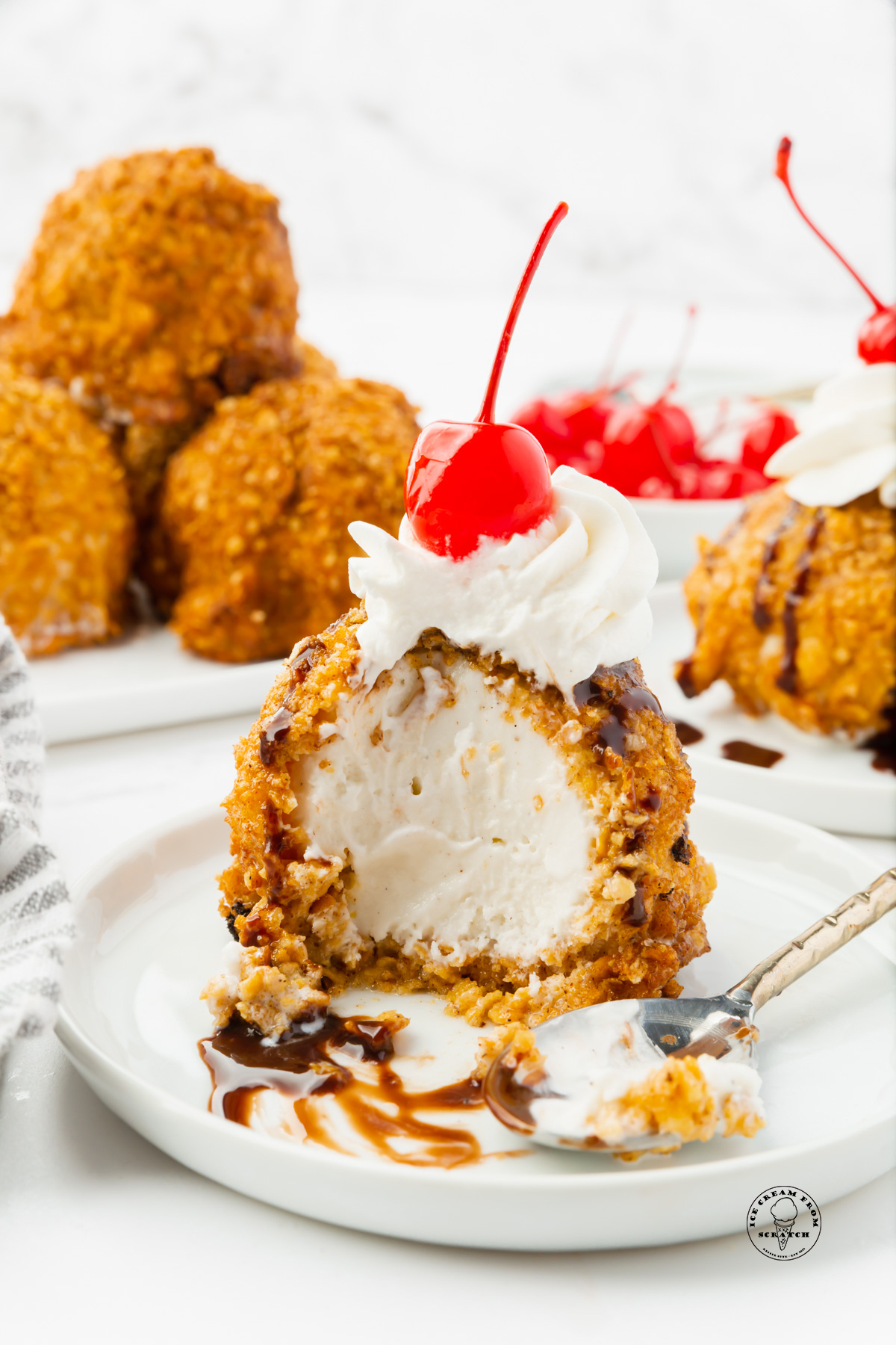 mexican fried ice cream on a plate, topped with whipped cream and a cherry. A spoon has taken a large bite from the dessert.