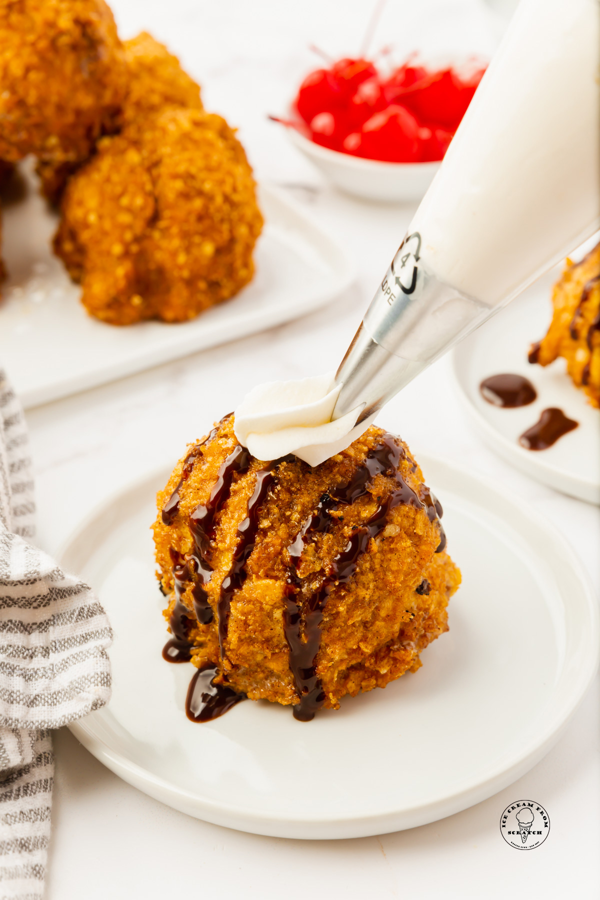 a piping bag adding whipped cream to a round scoop of fried ice cream.