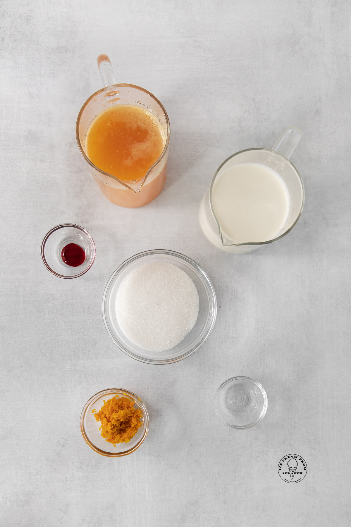 The ingredients needed for making orange sherbet, all in separate bowls and pitchers, arranged on a counter and viewed from above.