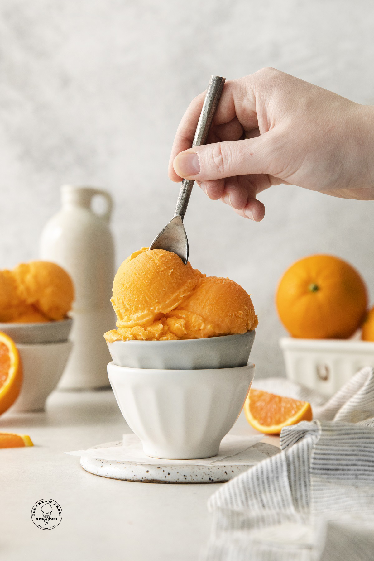 two small bowls stacked, filled with scoops of homemade orange sherbet. A hand is eating it with a small spoon.