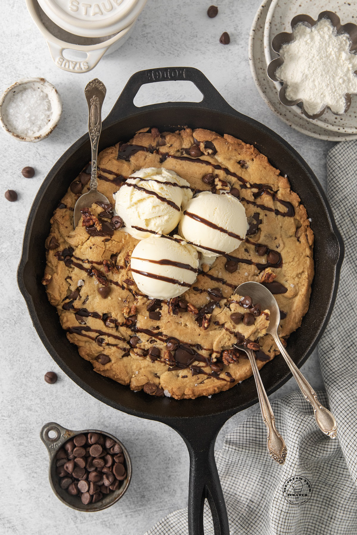 A giant cookie (pazookie) in a cast iron pan topped with scoops of ice cream. Three spoons are digging in.