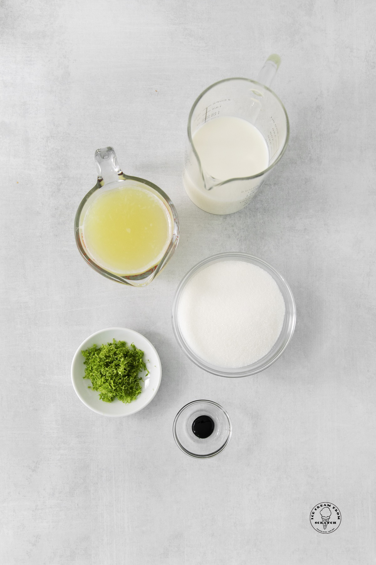 The ingredients for lime sherbet, including lime juice, sugar, and lime zest, all in separate measuring bowls, viewed from overhead.