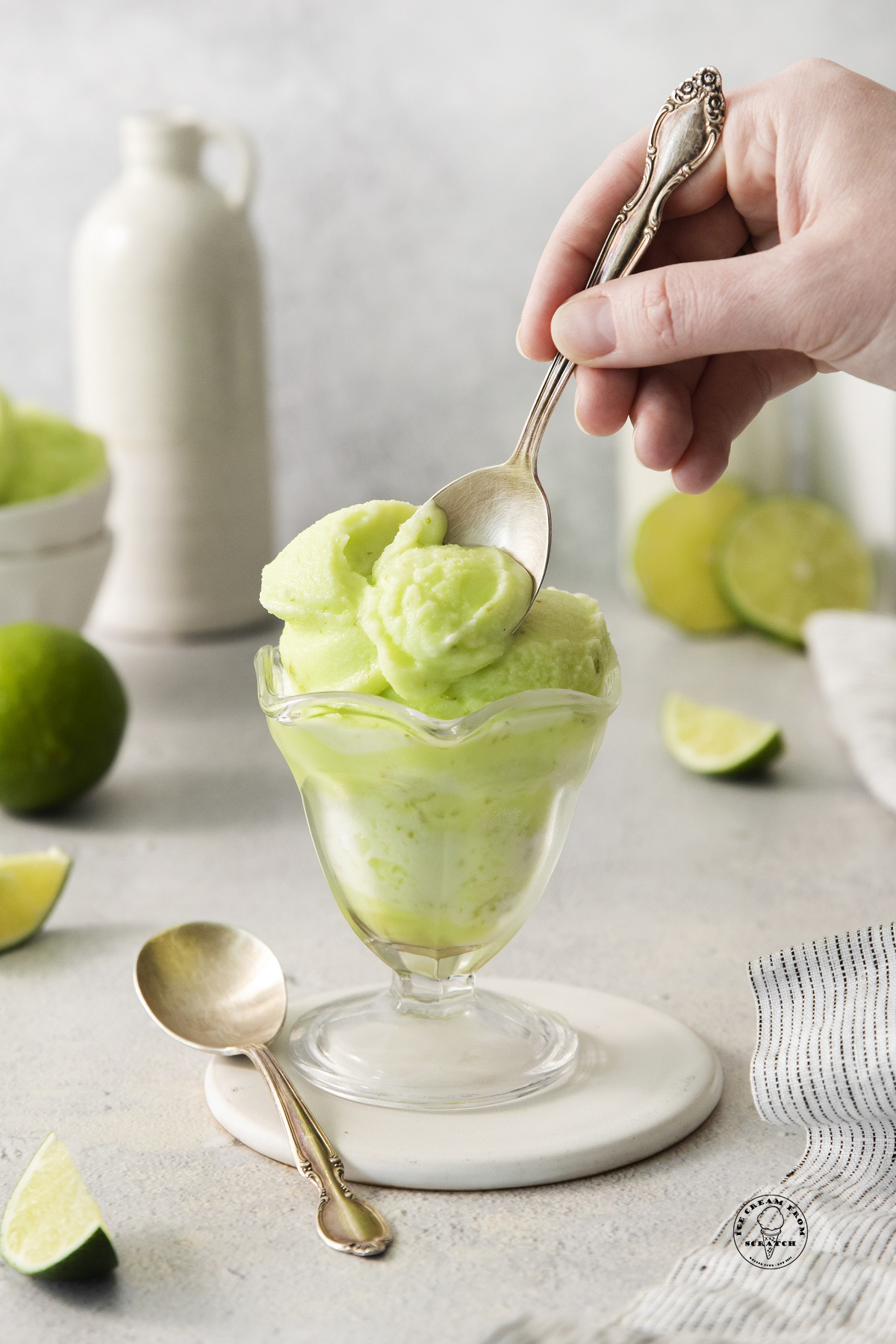 a hand holding a spoon and eating from a glass sundae glass filled with lime sherbet.