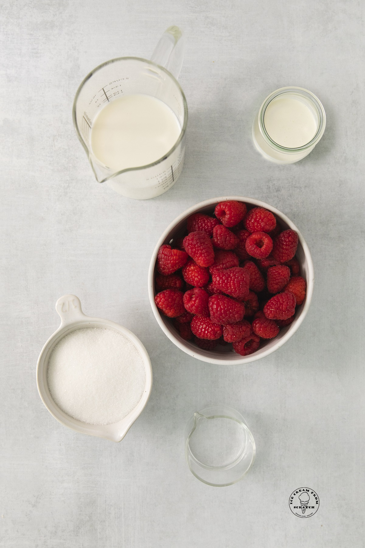 a bowl of fresh raspberries with milk, cream and sugar, all in separate bowls on a counter.