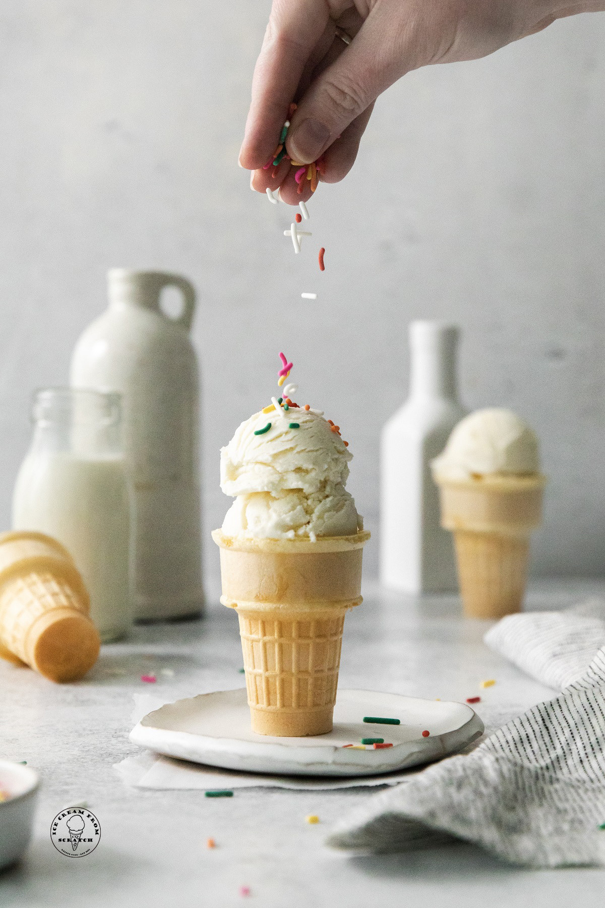 a cone of sugar free vanilla ice cream. A hand is adding sprinkles to the top.