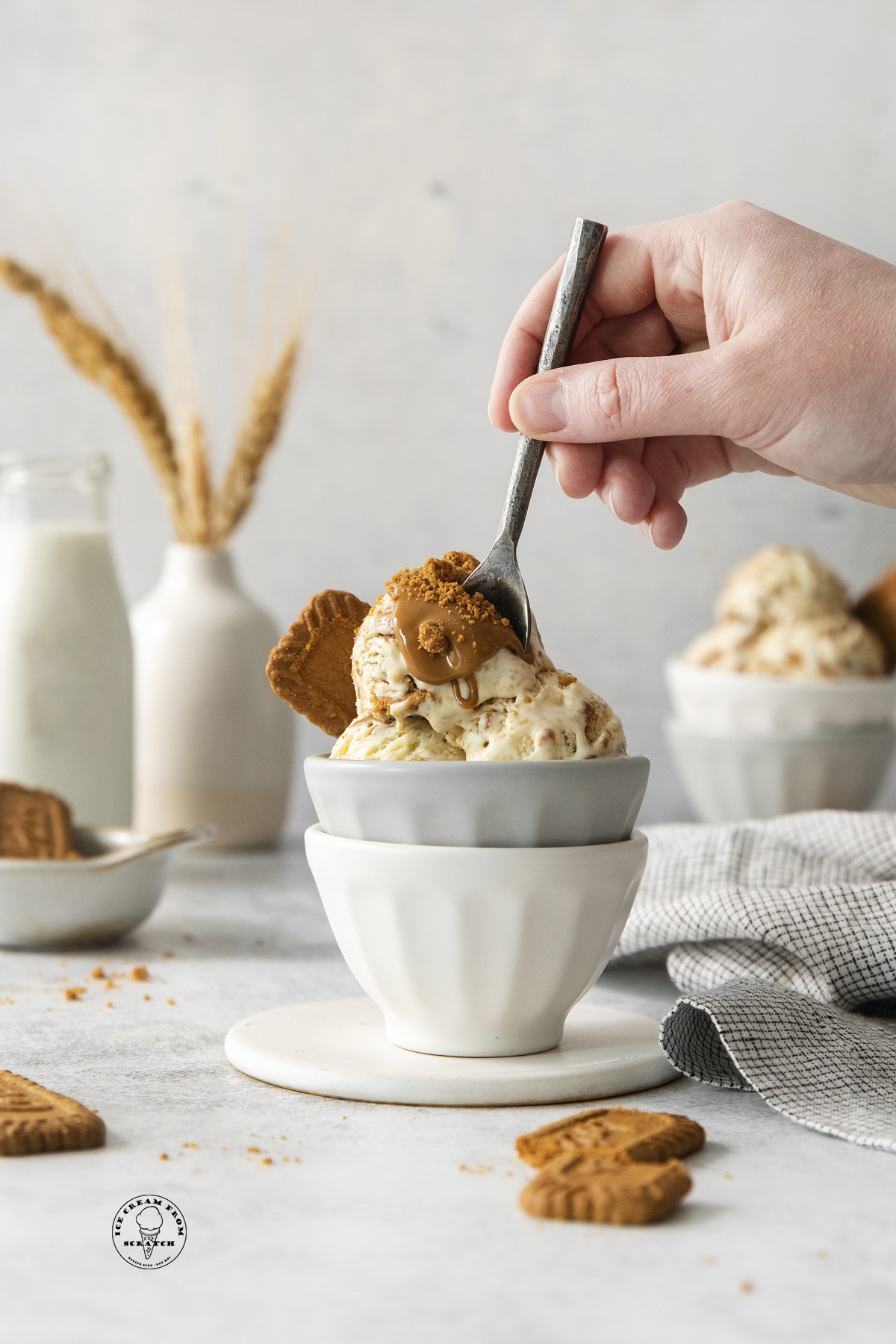 a hand holding a spoon that is digging into a bowl of homemade biscoff ice cream