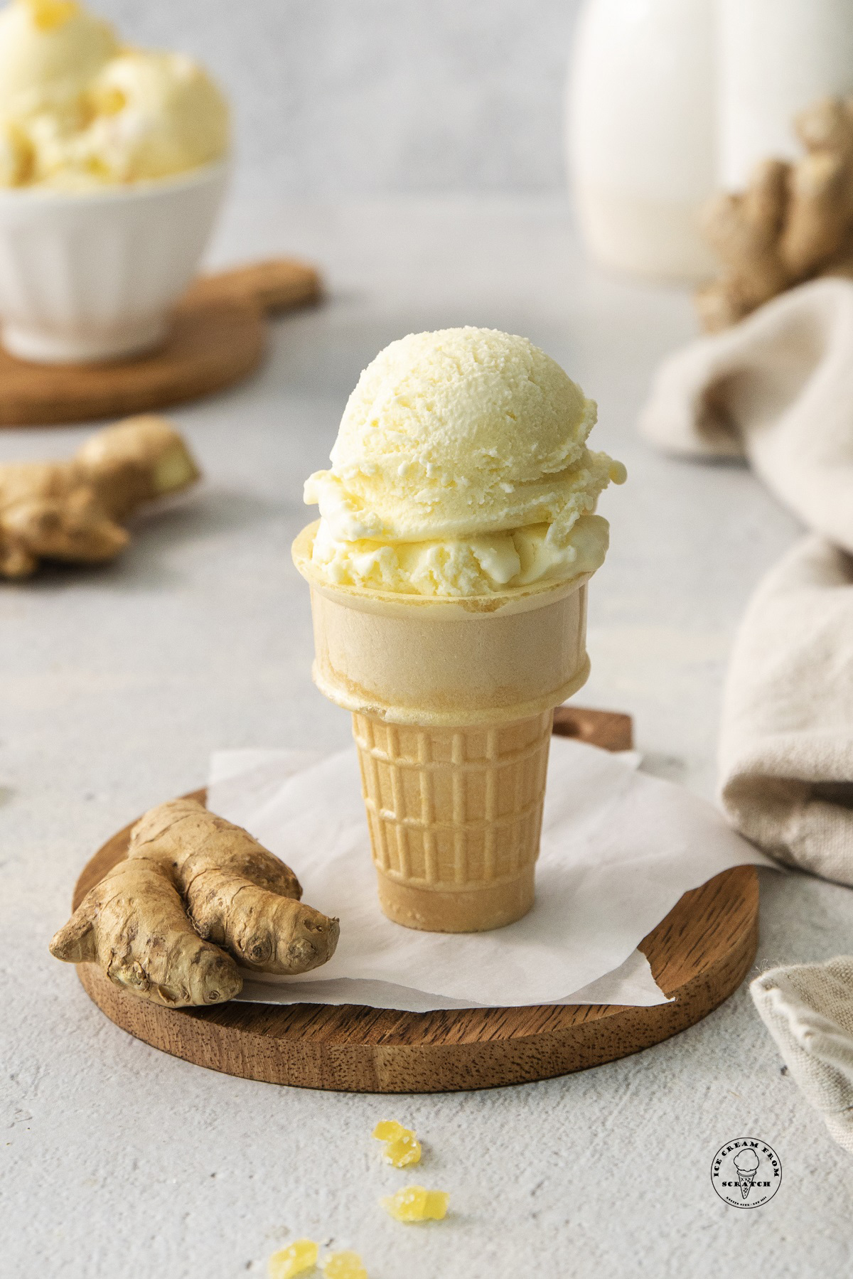 a cake cone with scoops of homemade ginger ice cream next to a piece of fresh ginger.