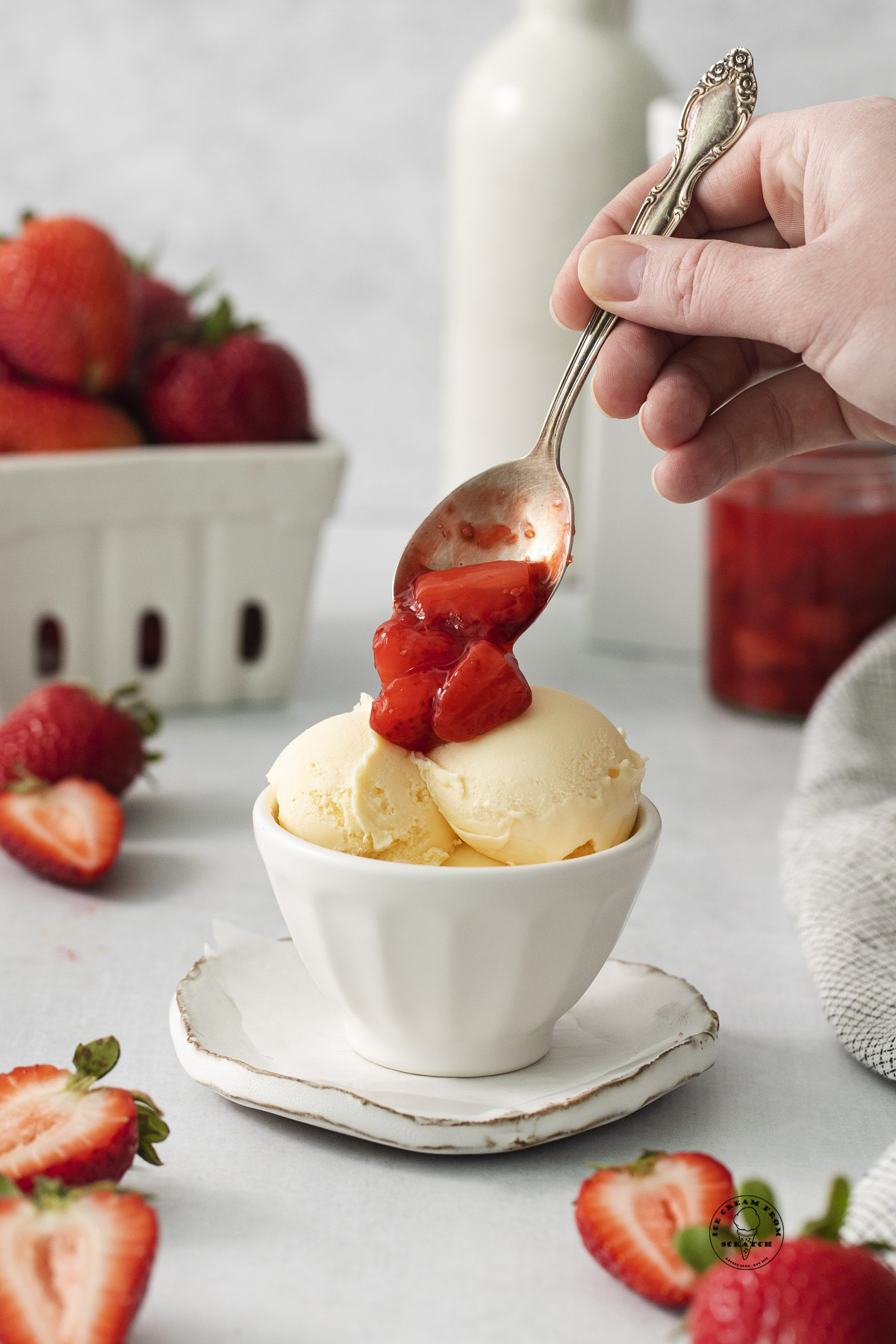 a hand spooning strawberry compote over scoops of vanilla ice cream.