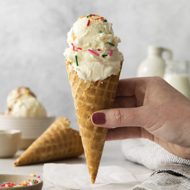 vanilla anabolic ice cream in a sugar cone, topped with sprinkles, held by a hand.