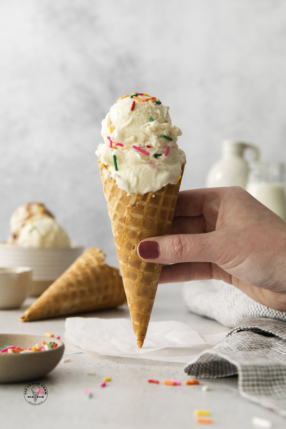 vanilla anabolic ice cream in a sugar cone, topped with sprinkles, held by a hand.