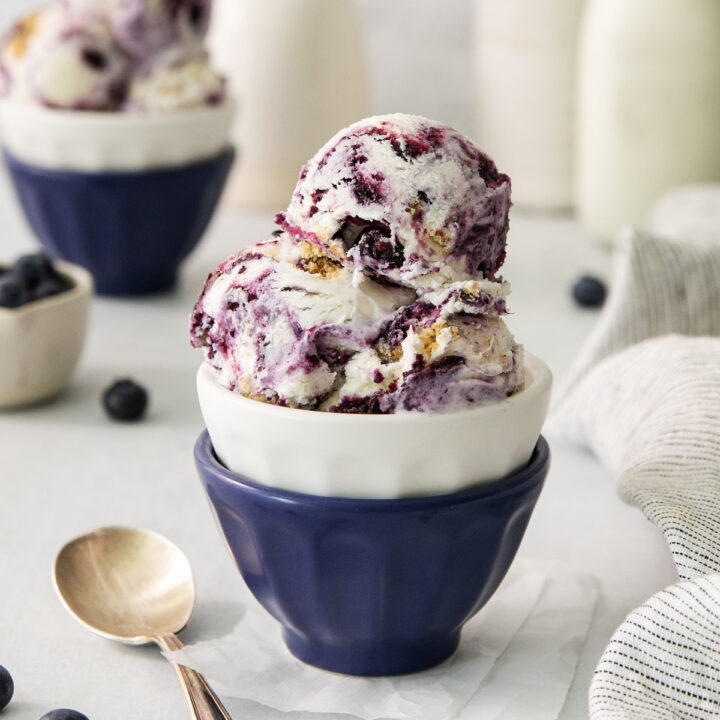 scoops of blueberry cheesecake ice cream in a blue ceramic bowl.