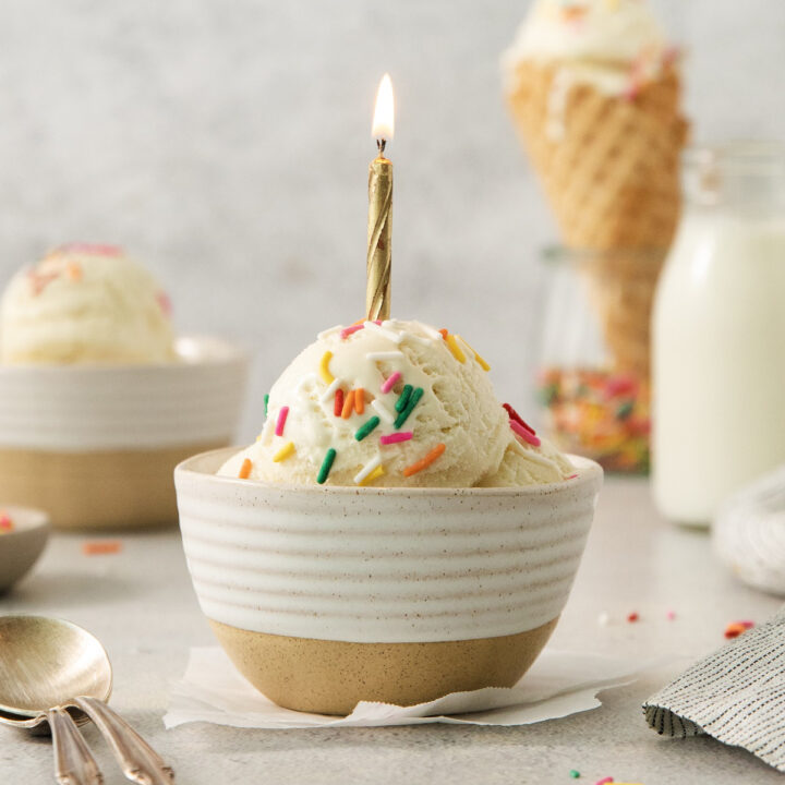 a ceramic bowl with scoops of ice cream, topped with sprinkles and a lit birthday candle.