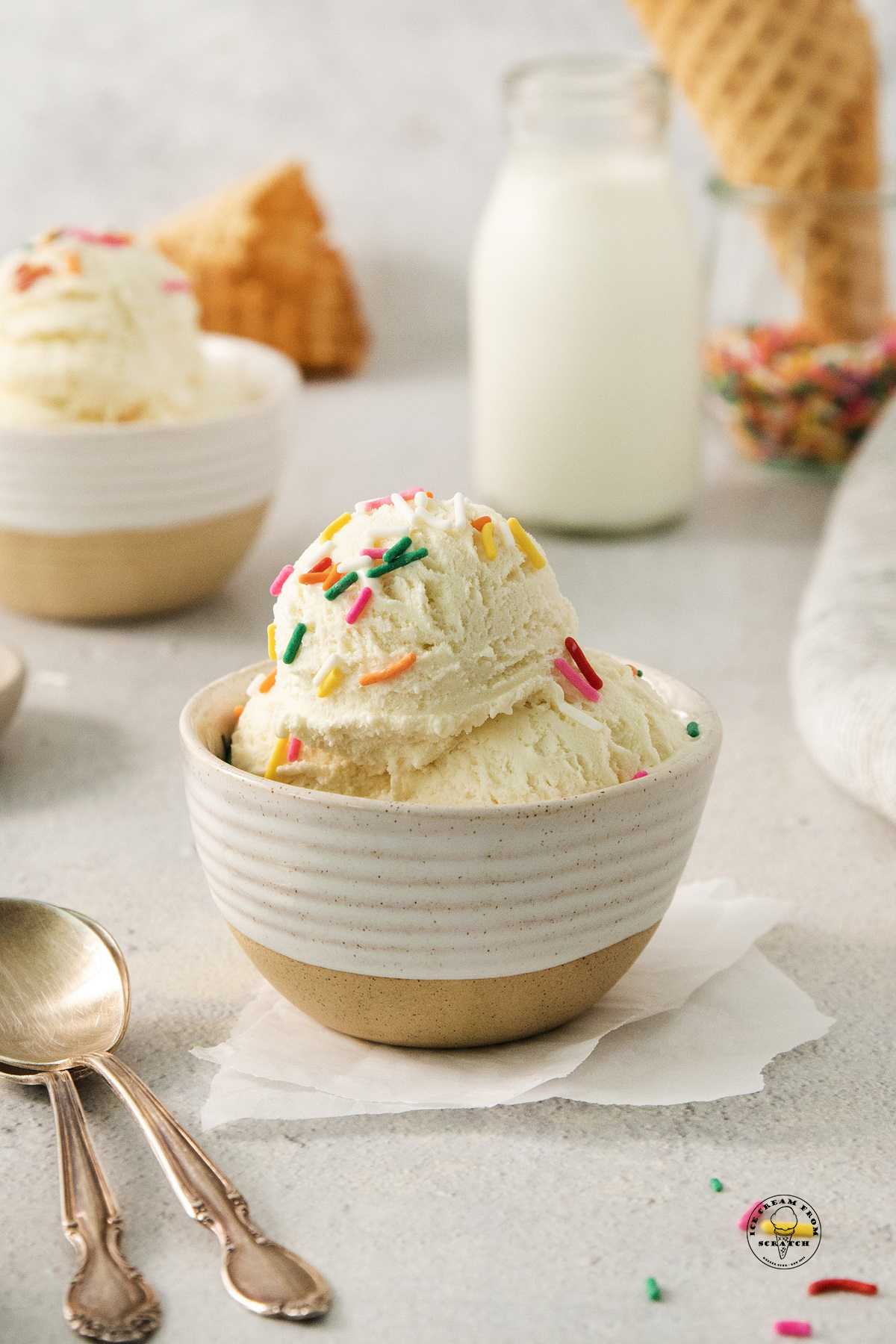 a ceramic bowl filled with scoops of cake batter ice cream, topped with rainbow sprinkles