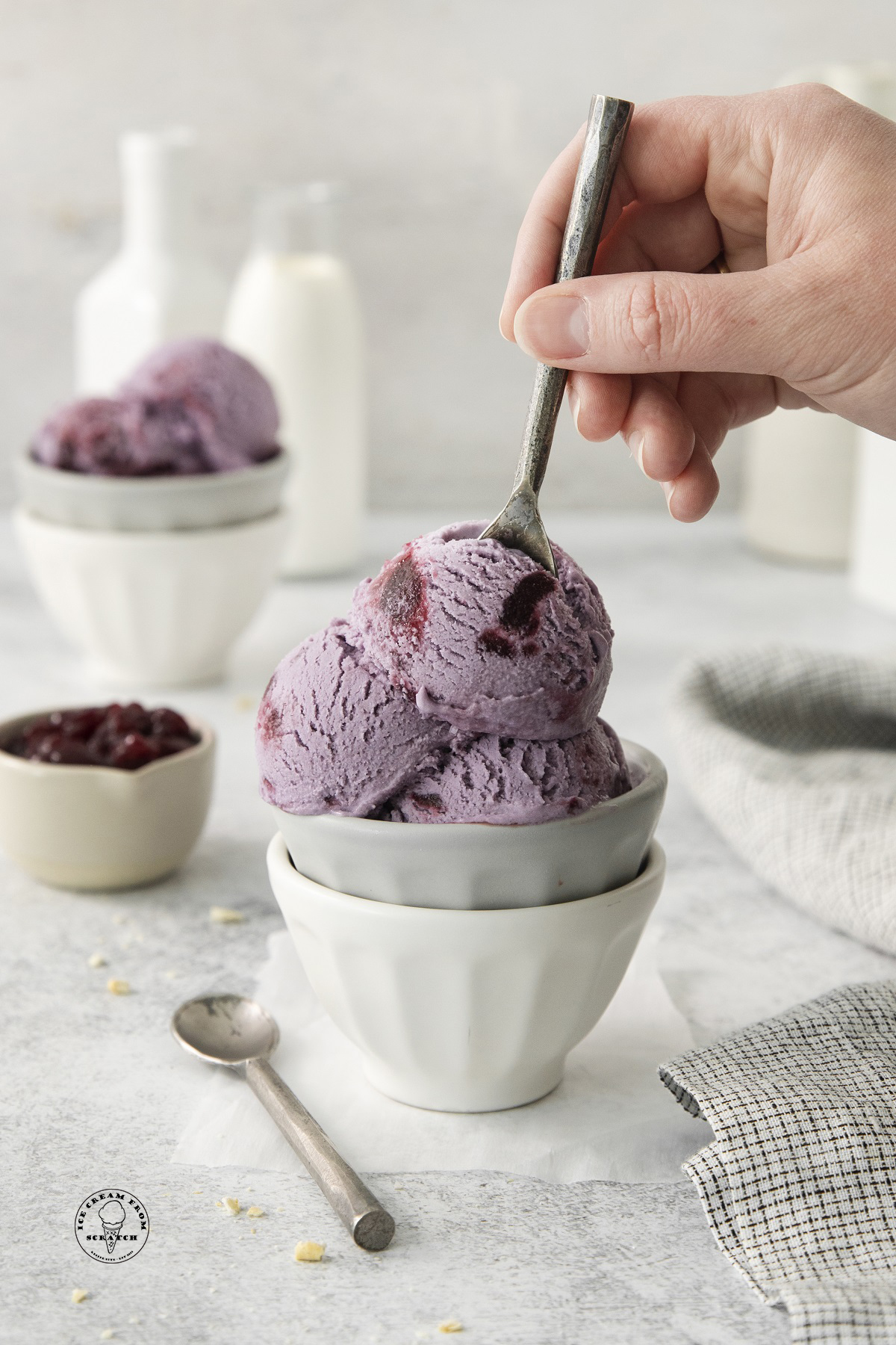 a bowl filled with scoops of grape ice cream. a hand is eating it with a small spoon