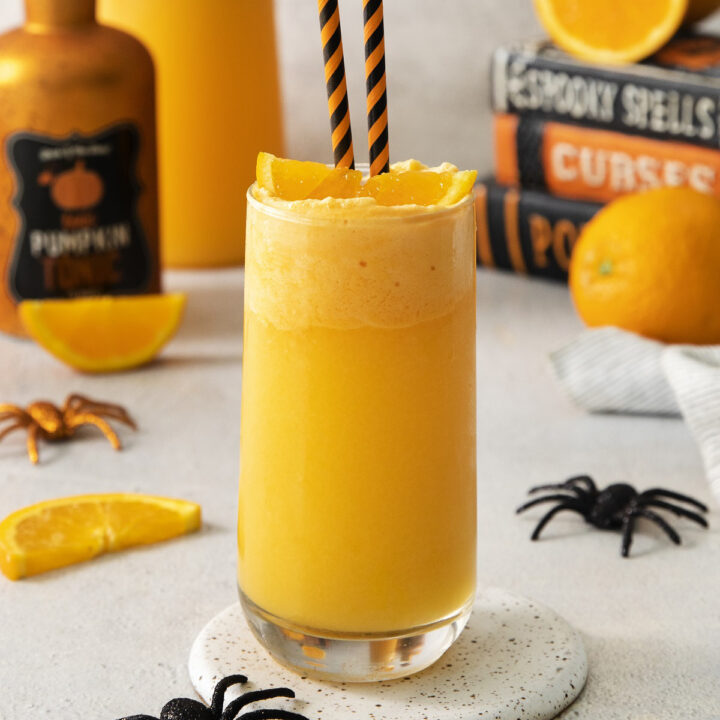 Orange halloween punch in a glass. Halloween decorations are in the background.