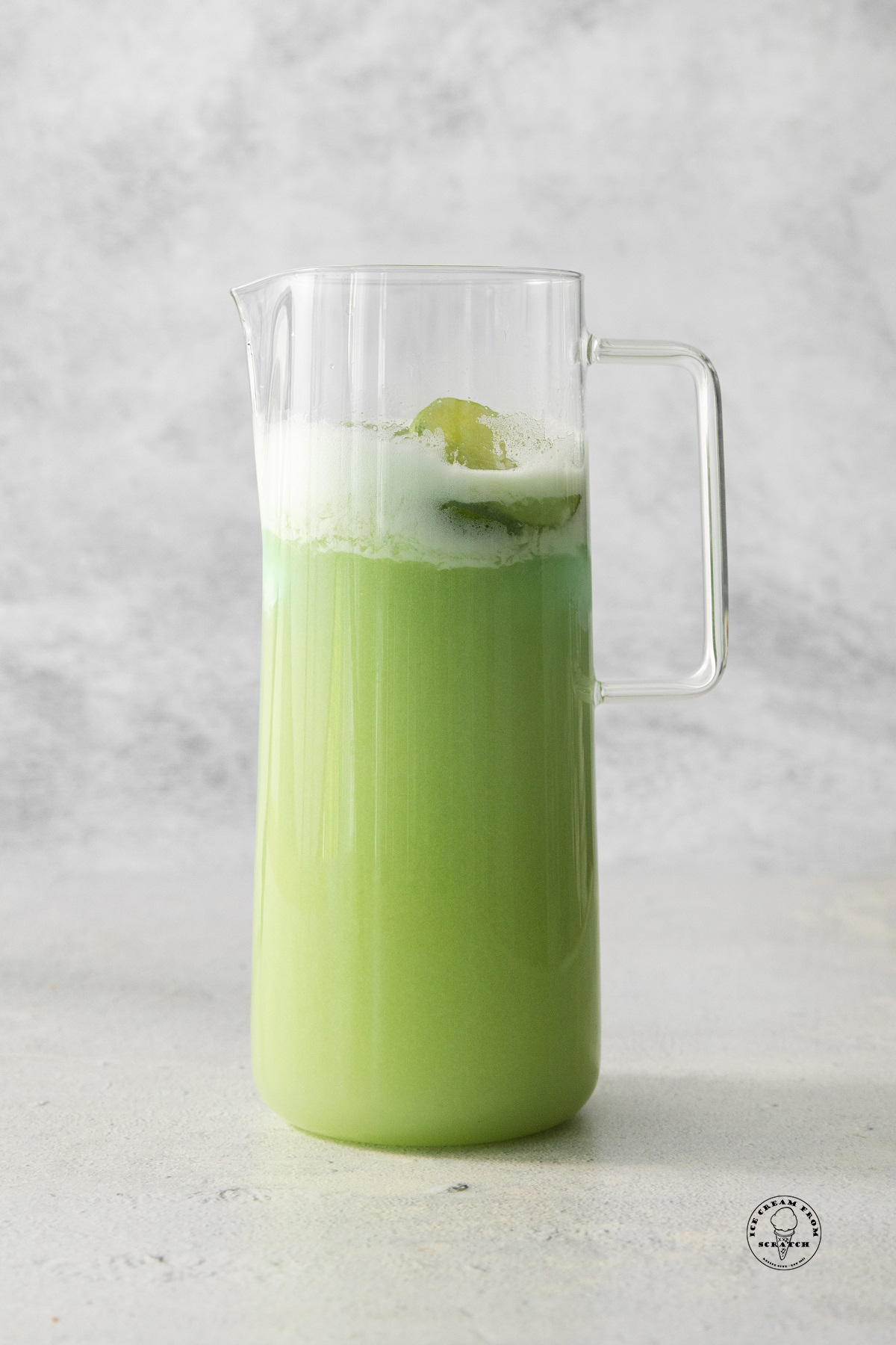 a tall glass pitcher filled with green lime sherbet punch with foam on top.