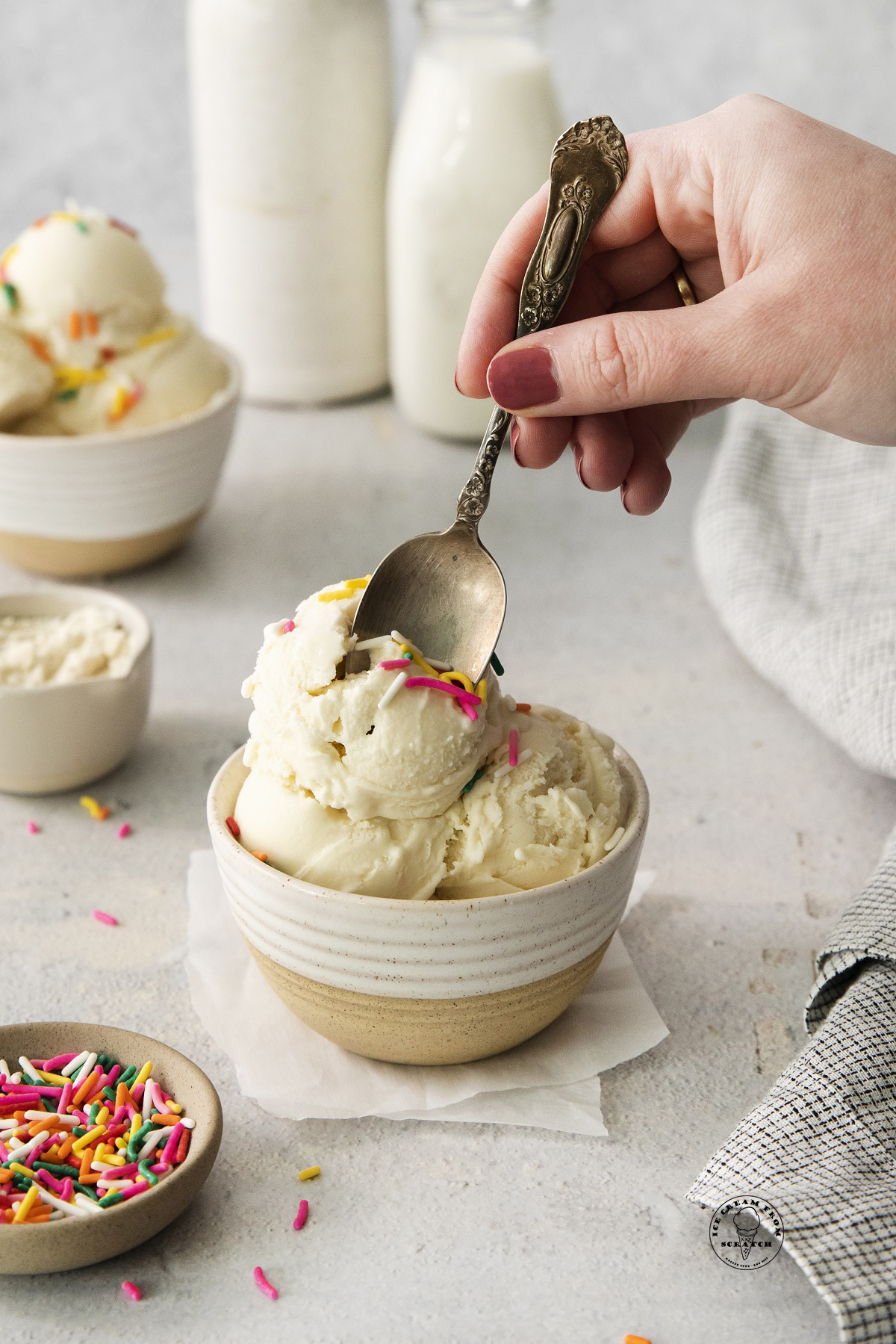 a hand holding a silver spoon, eating a bowl of protein ice cream with sprinkles.