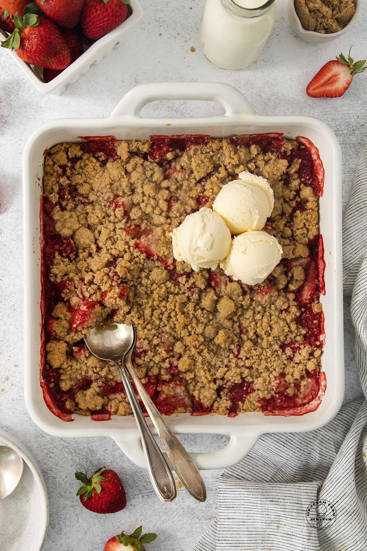 a white square baking dish of strawberry crumble with three scoops of ice cream at the top cornder.