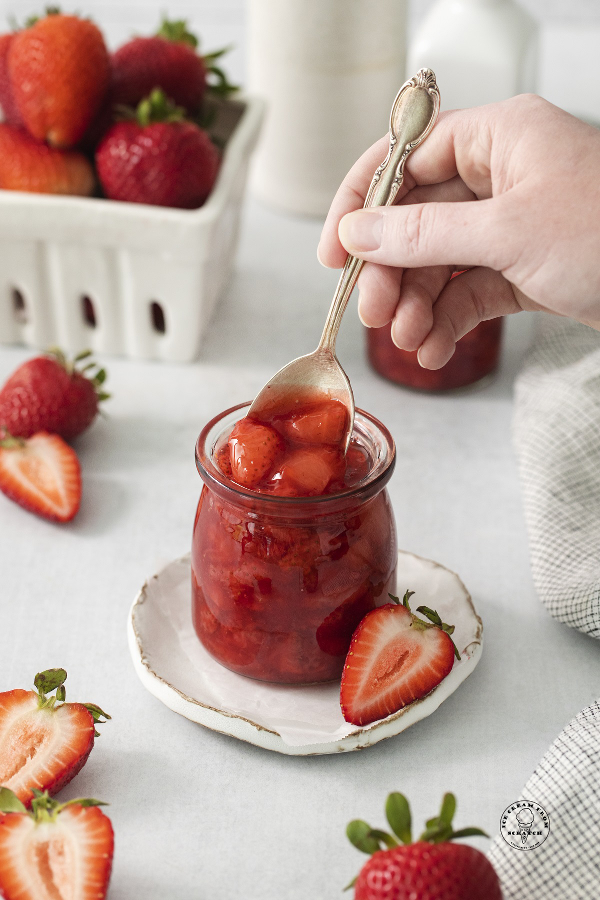a small jar of strawberry compote. A hand is spooning it out of the jar.