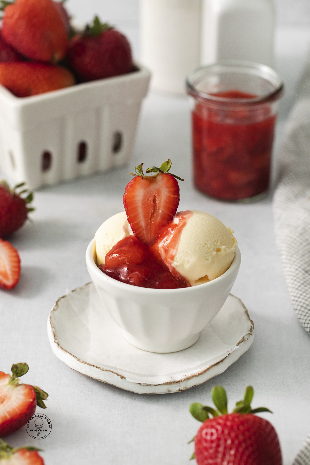 a small bowl of scoops of vanilla ice cream, topped with strawberry compote and half a fresh strawberry