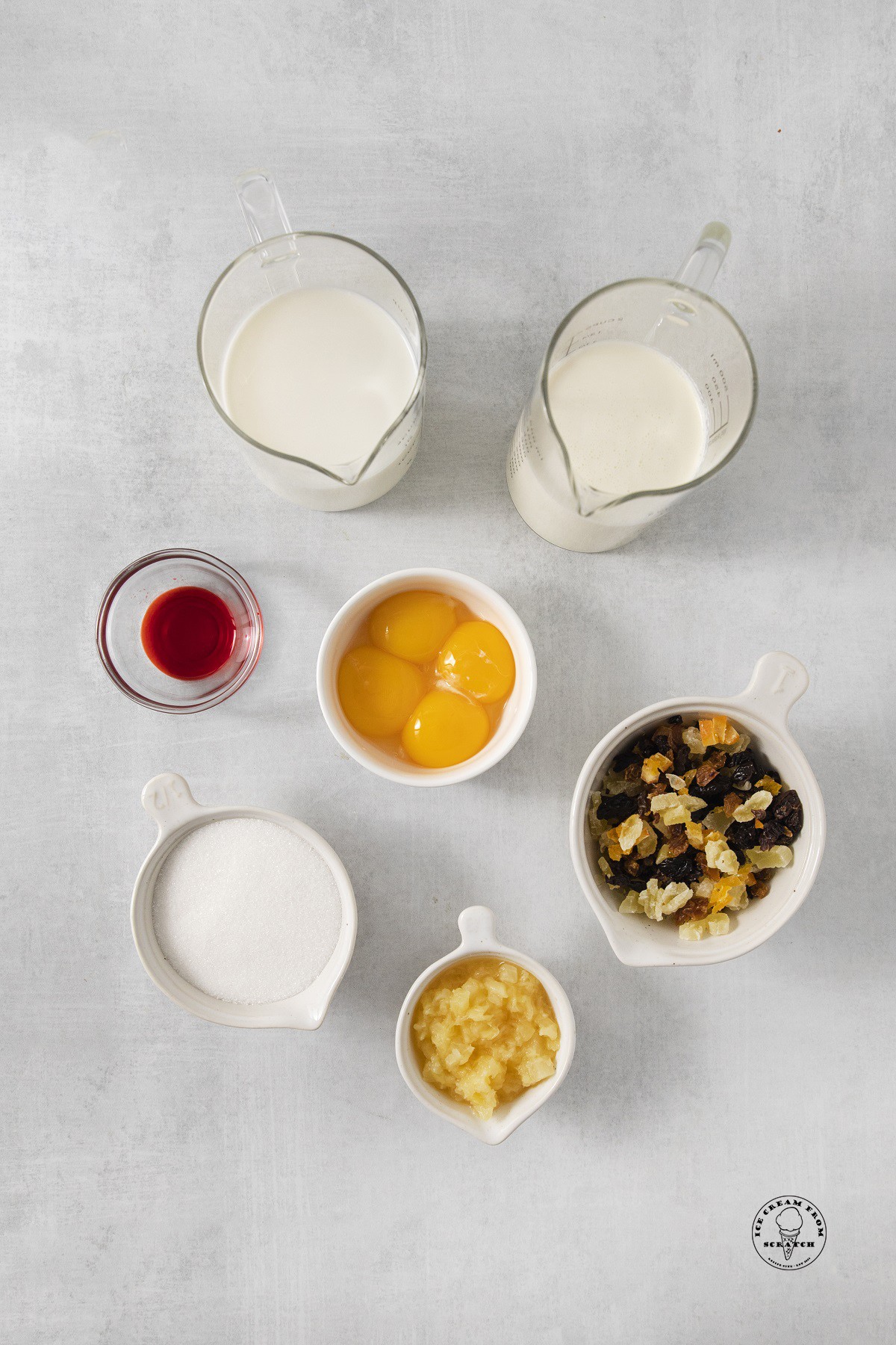The ingredients needed to make a french style tutti frutti ice cream recipe, with dried fruit, egg yolks, sugar, and milk, all measured out into individual containers.