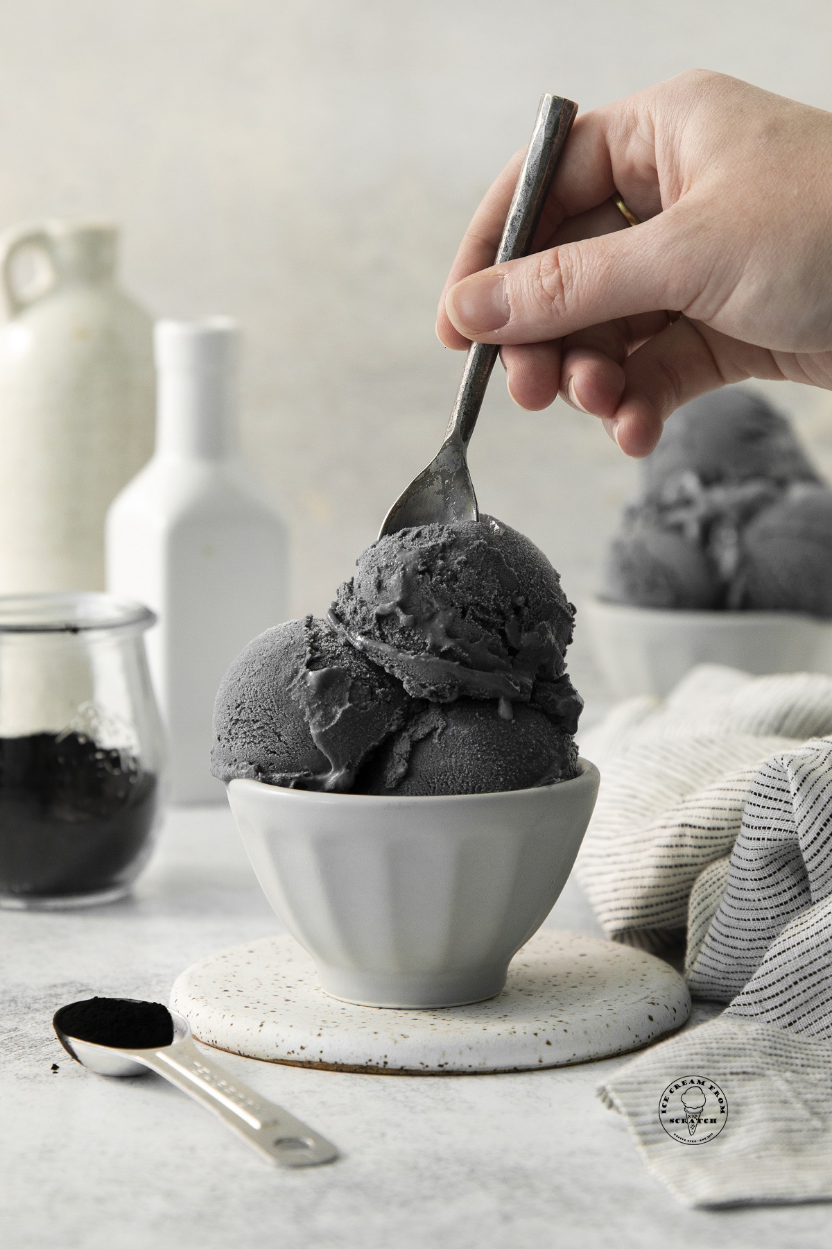 scoops of black ice cream in a bowl, a hand is eating it with a spoon.