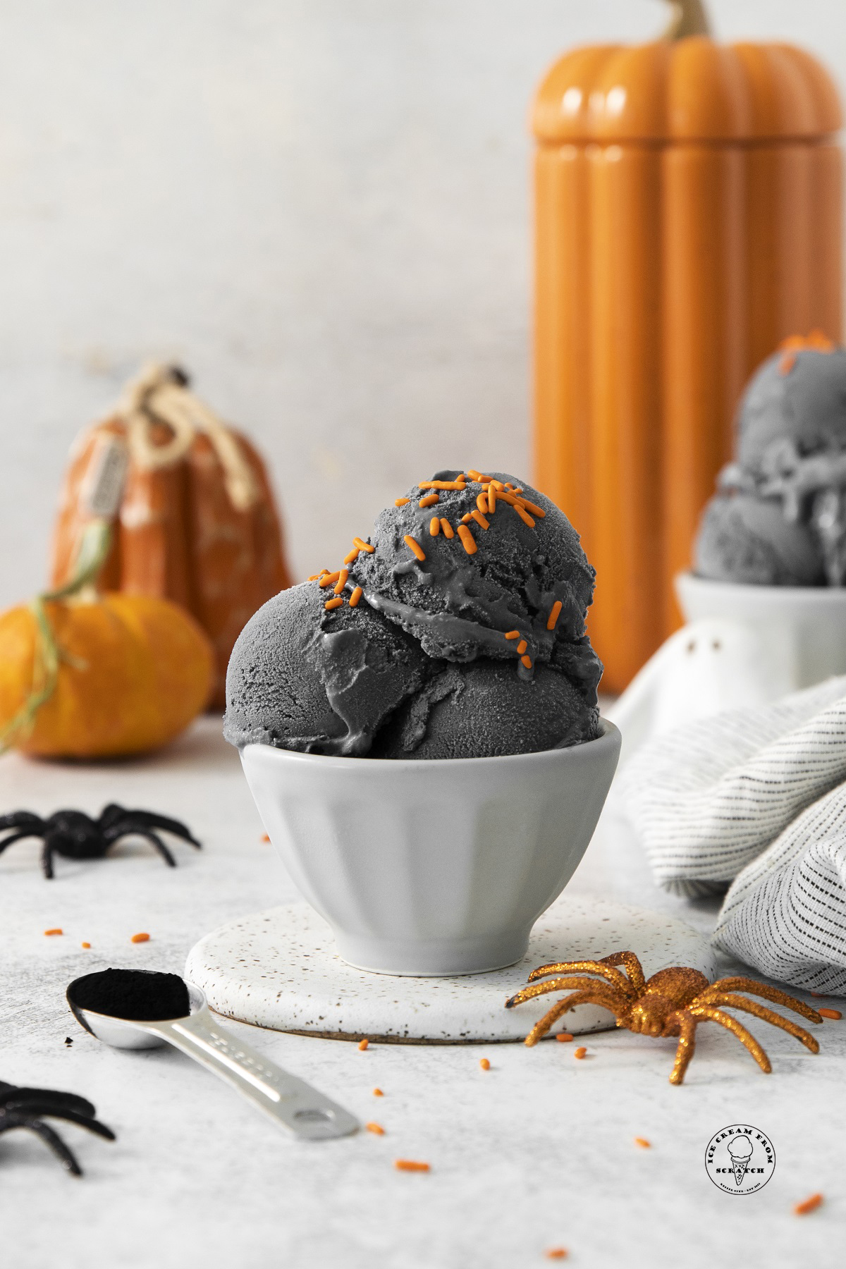 a bowl of black ice cream with orange sprinkles and halloween decorations in the background.
